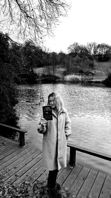 April E Swan holding Autumn Reads book in front of a lake 